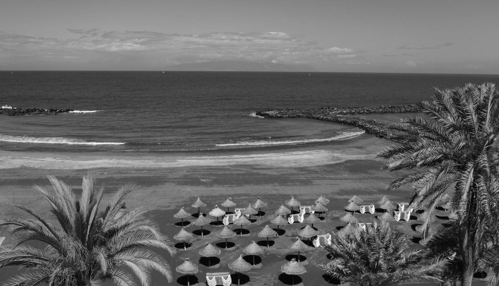 a black and white photo of a swimming pool with chairs and umbrellas=s1900