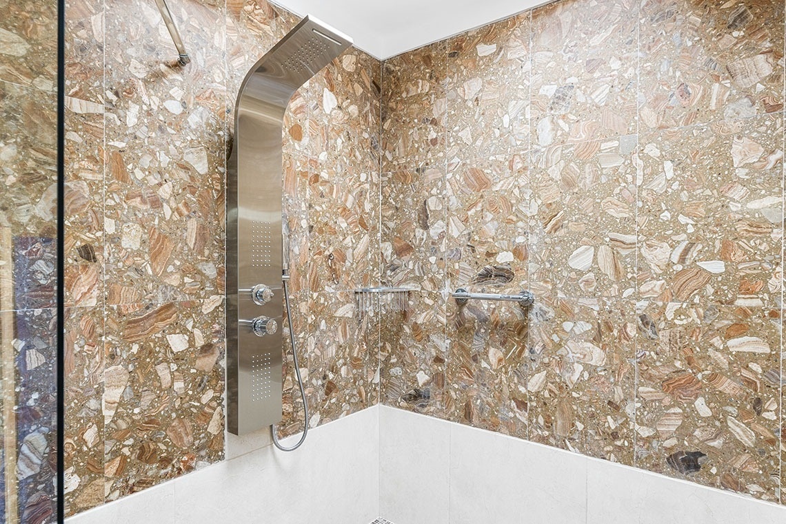 a shower with a marble wall and a stainless steel shower head