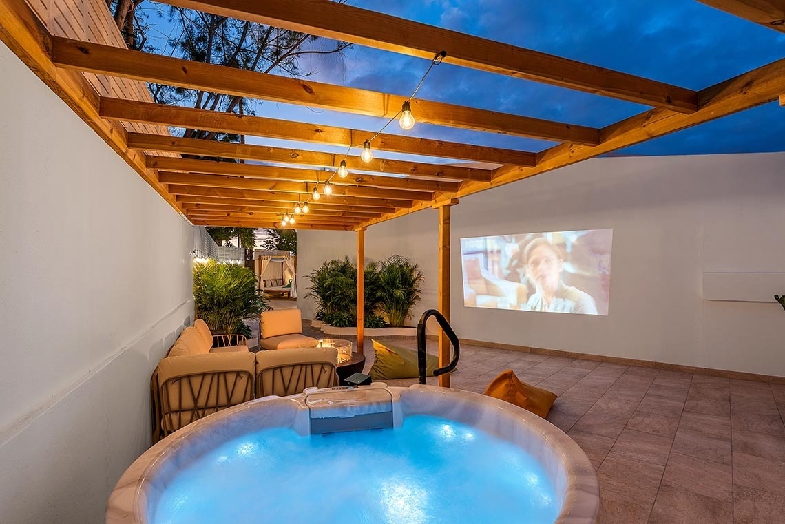 a hot tub under a pergola with a projector screen behind it