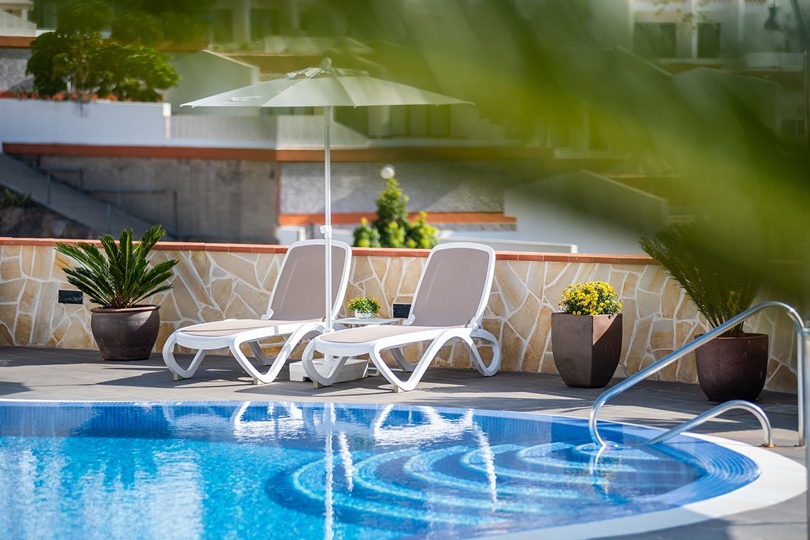 dos tumbonas y un paraguas junto a una piscina