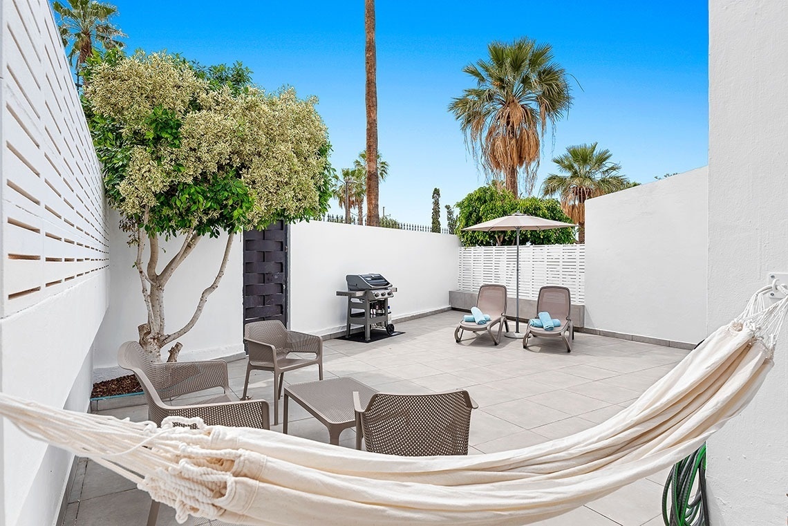 a patio with a hammock and chairs and a grill