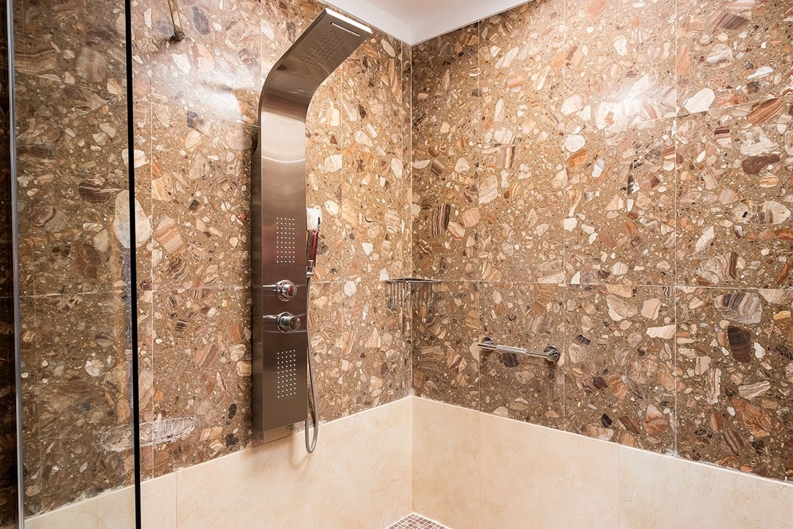 a shower with a marble wall and a stainless steel shower head
