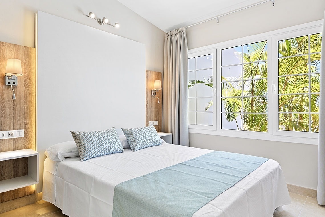 a bedroom with a bed and a window with palm trees in the background