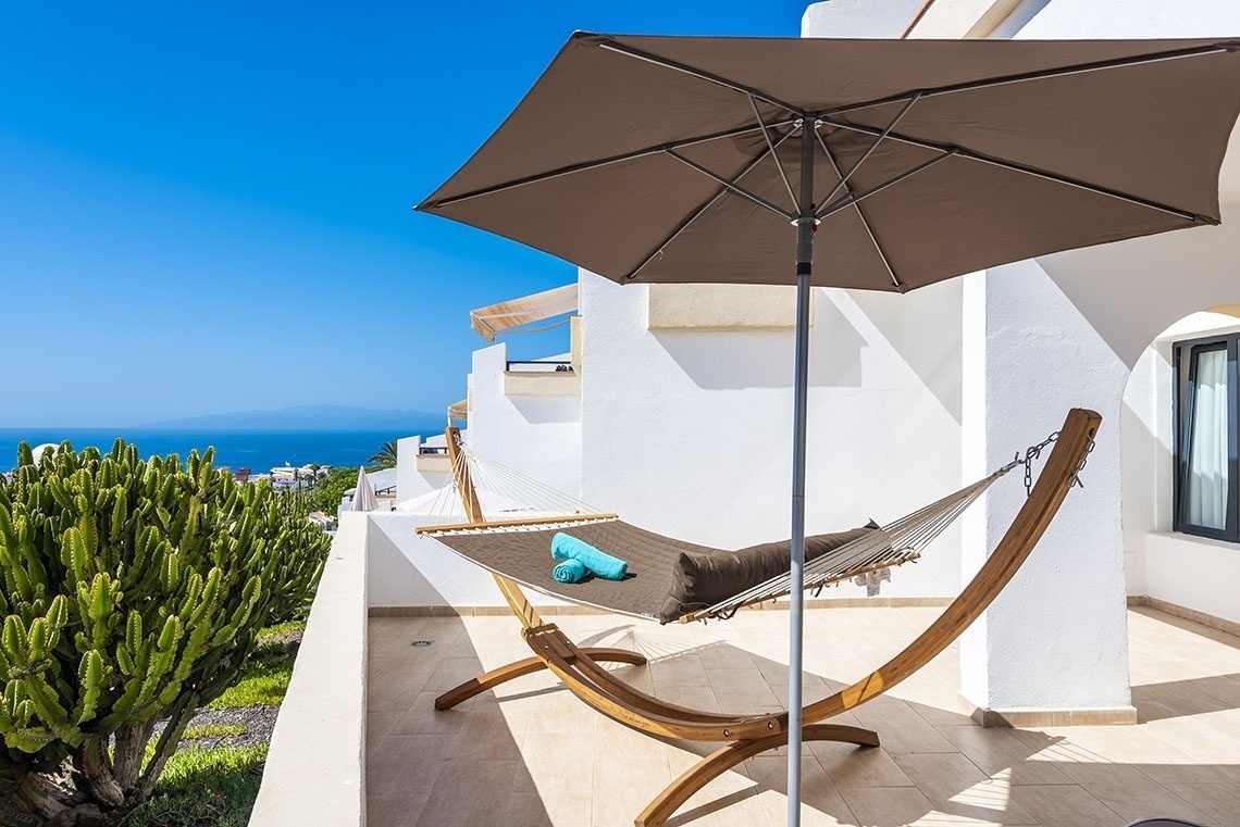 a hammock sits under an umbrella on a balcony overlooking the ocean