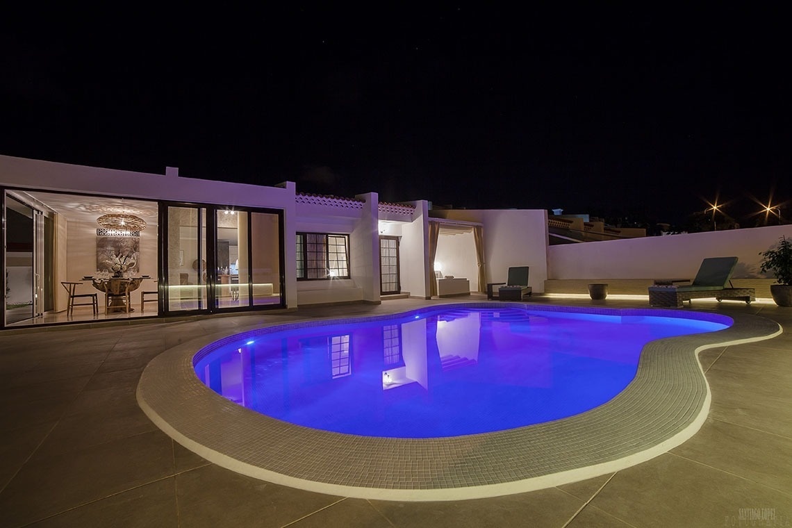 a swimming pool is lit up at night in front of a house