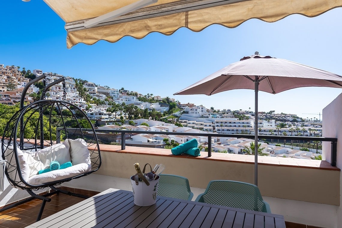 a balcony with a pink umbrella and a hanging chair