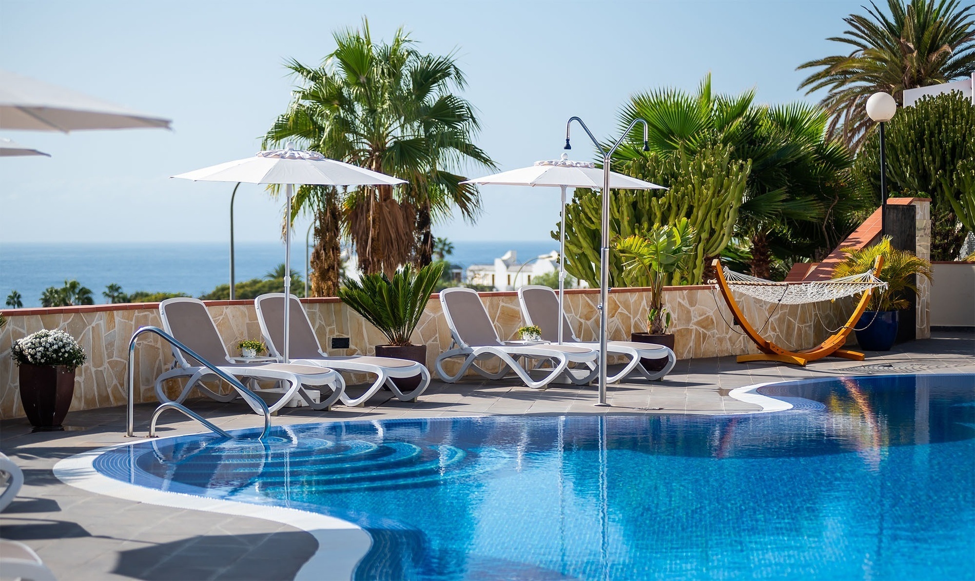 una piscina rodeada de sillas y sombrillas con vistas al océano