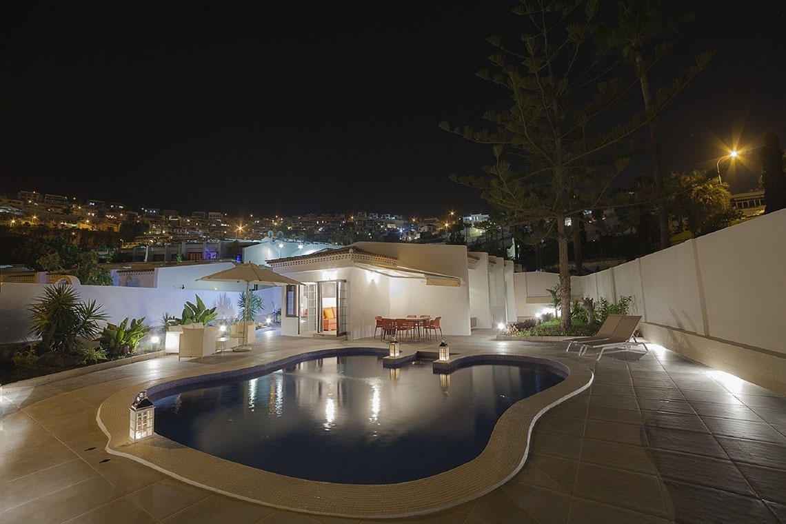a large swimming pool in front of a house at night