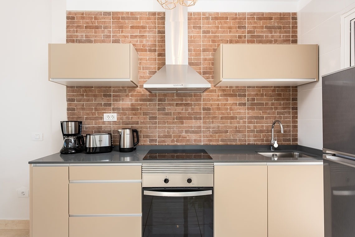 a kitchen with tan cabinets and a brick wall