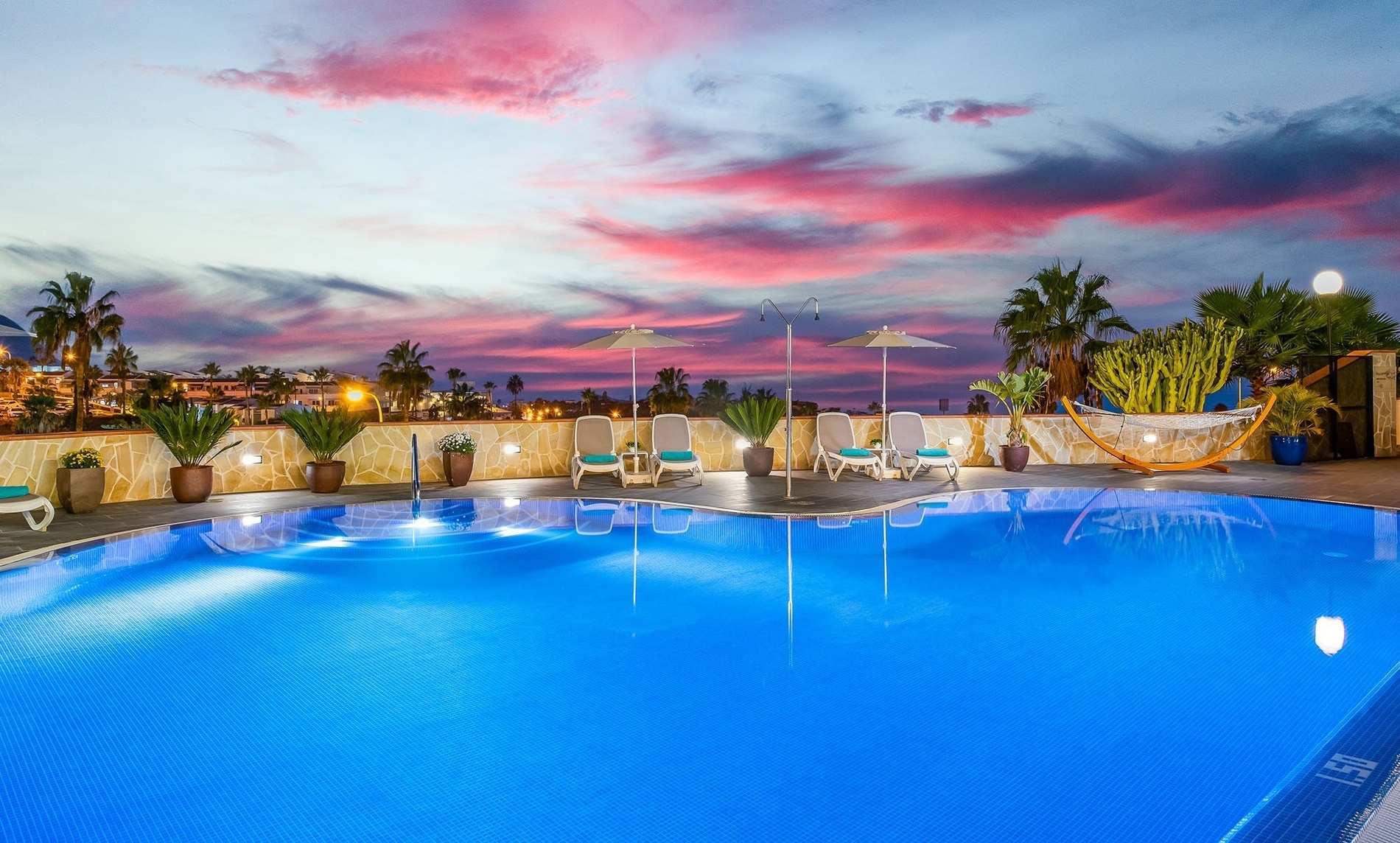 une piscine avec des chaises et des parasols au coucher du soleil