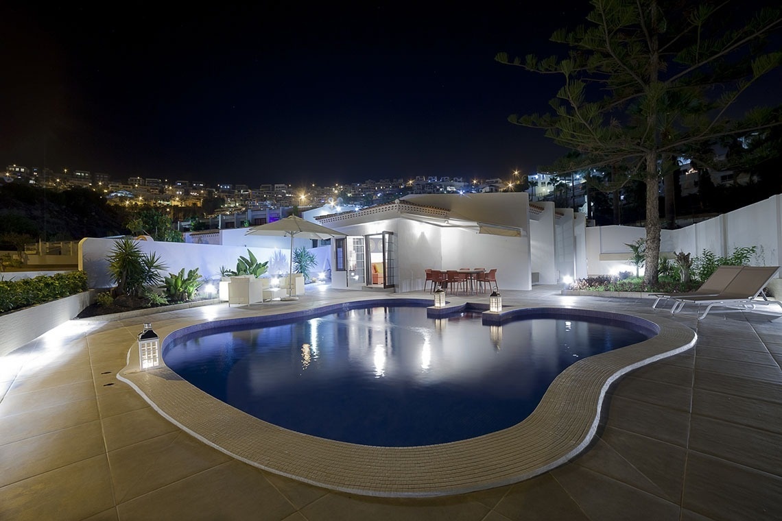a large swimming pool in front of a house at night