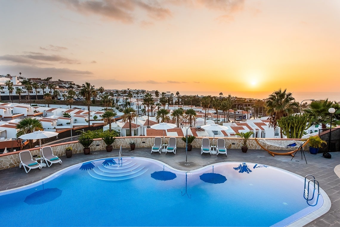 una piscina con sillas y sombrillas alrededor al atardecer