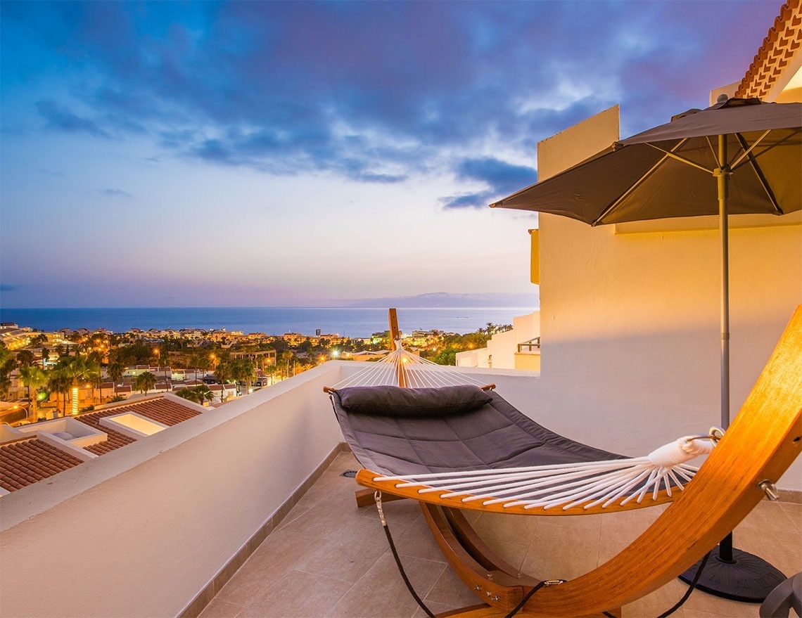 una hamaca y un paraguas en un balcón con vista al océano