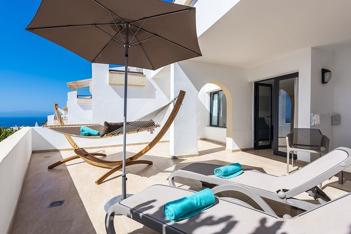 a hammock and lounge chairs on a balcony with an umbrella