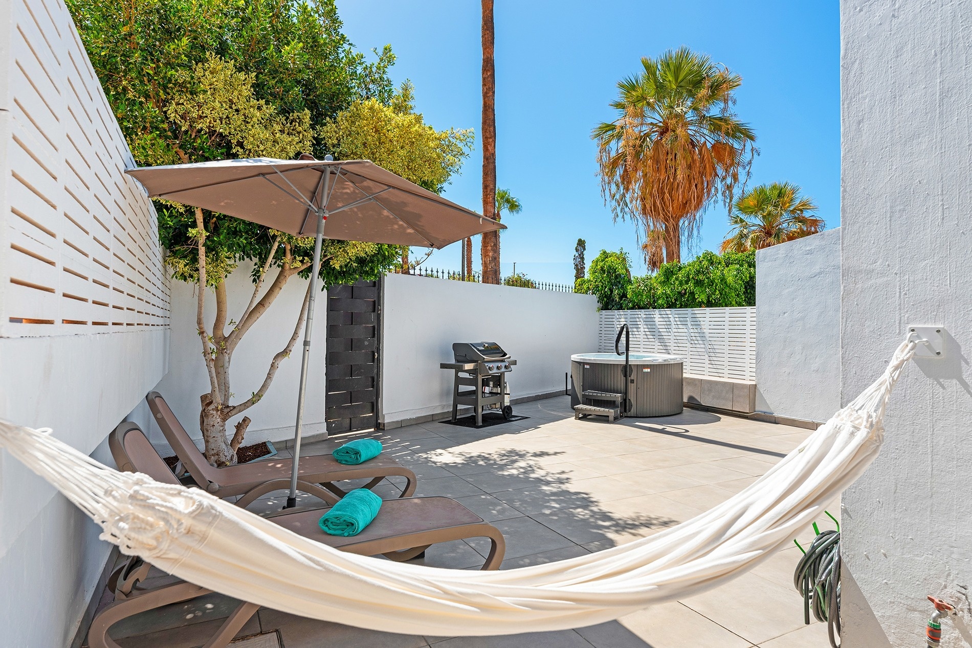 a patio with a hammock and chairs and a hot tub