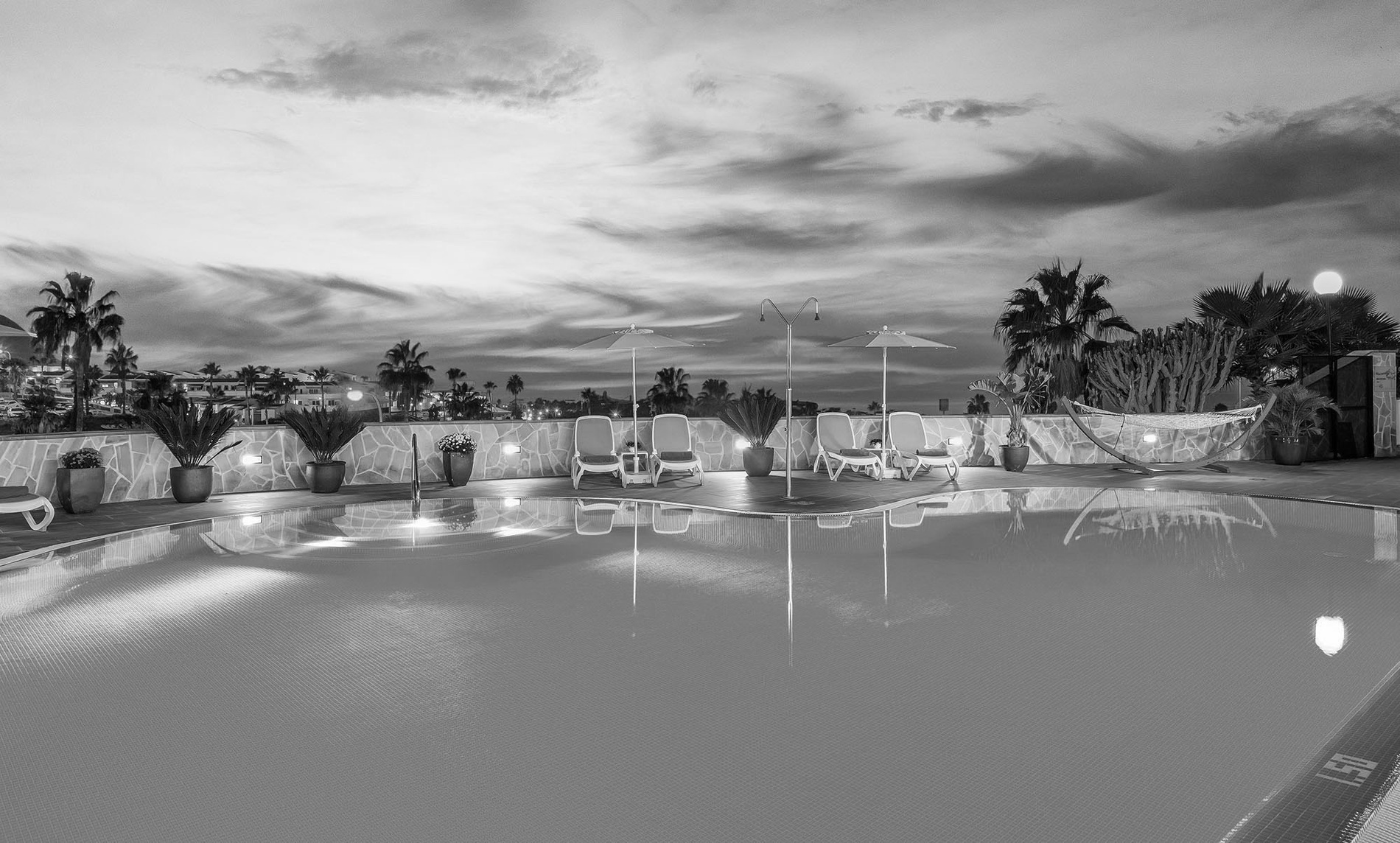 una piscina circondata da sedie e ombrelloni è illuminata al tramonto=s1900