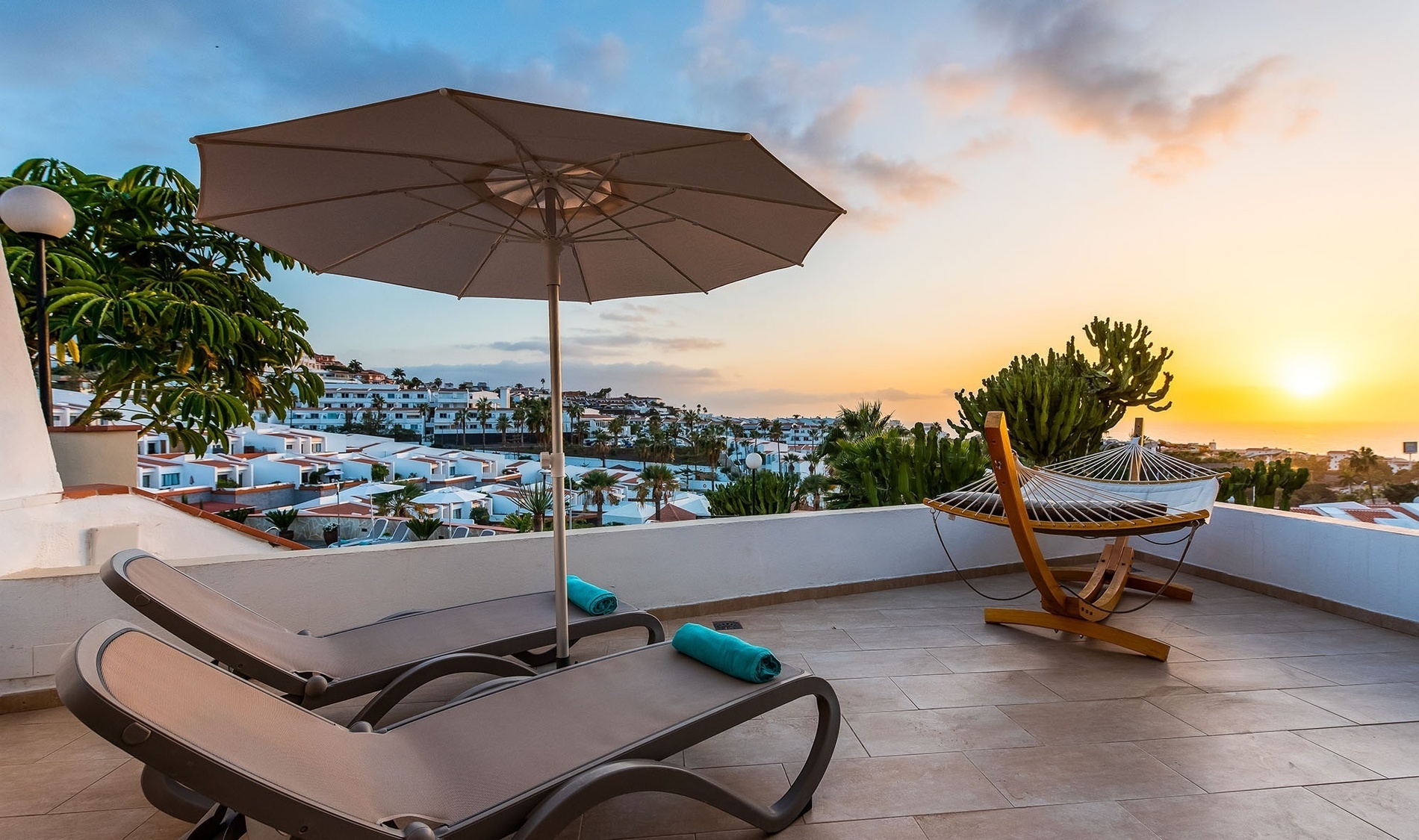 two lounge chairs under an umbrella with a hammock in the background