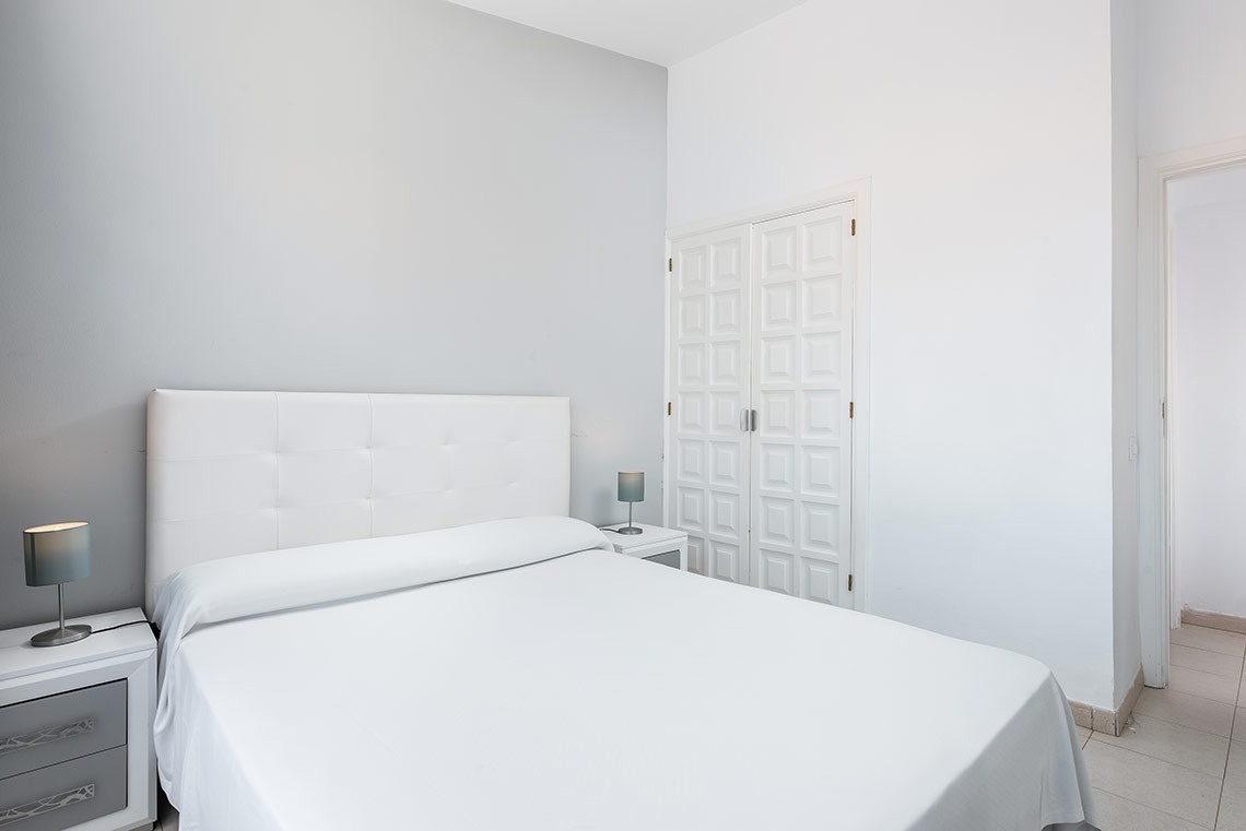 una habitación blanca con una cama y dos mesitas de noche