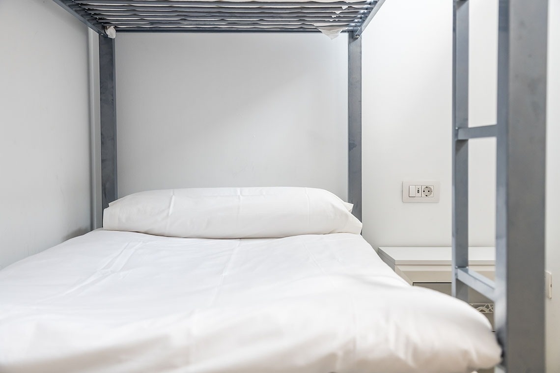 un letto a castello con lenzuola bianche e una presa elettrica