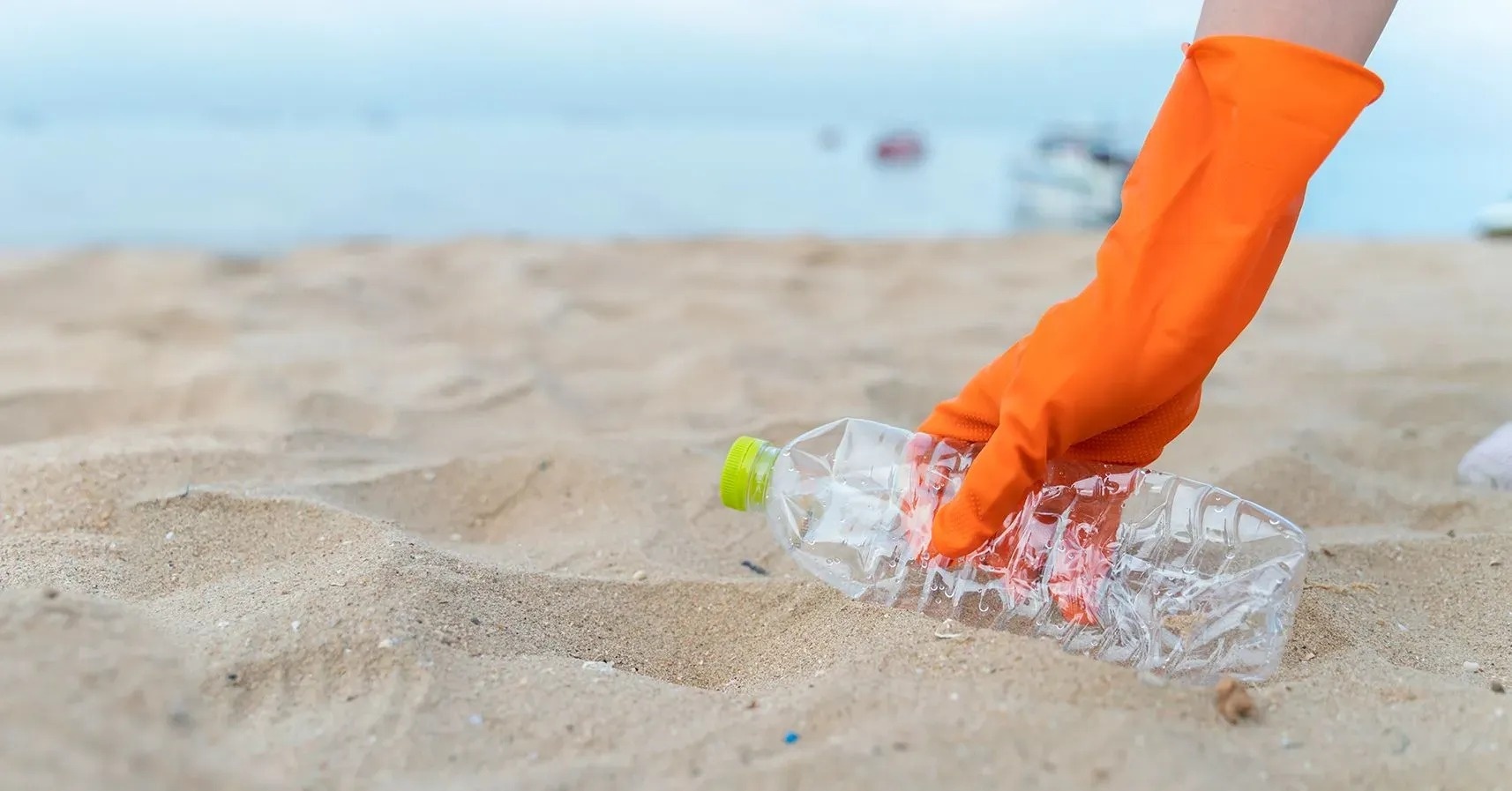 una persona con guantes naranjas recoge una botella de plástico en la playa
