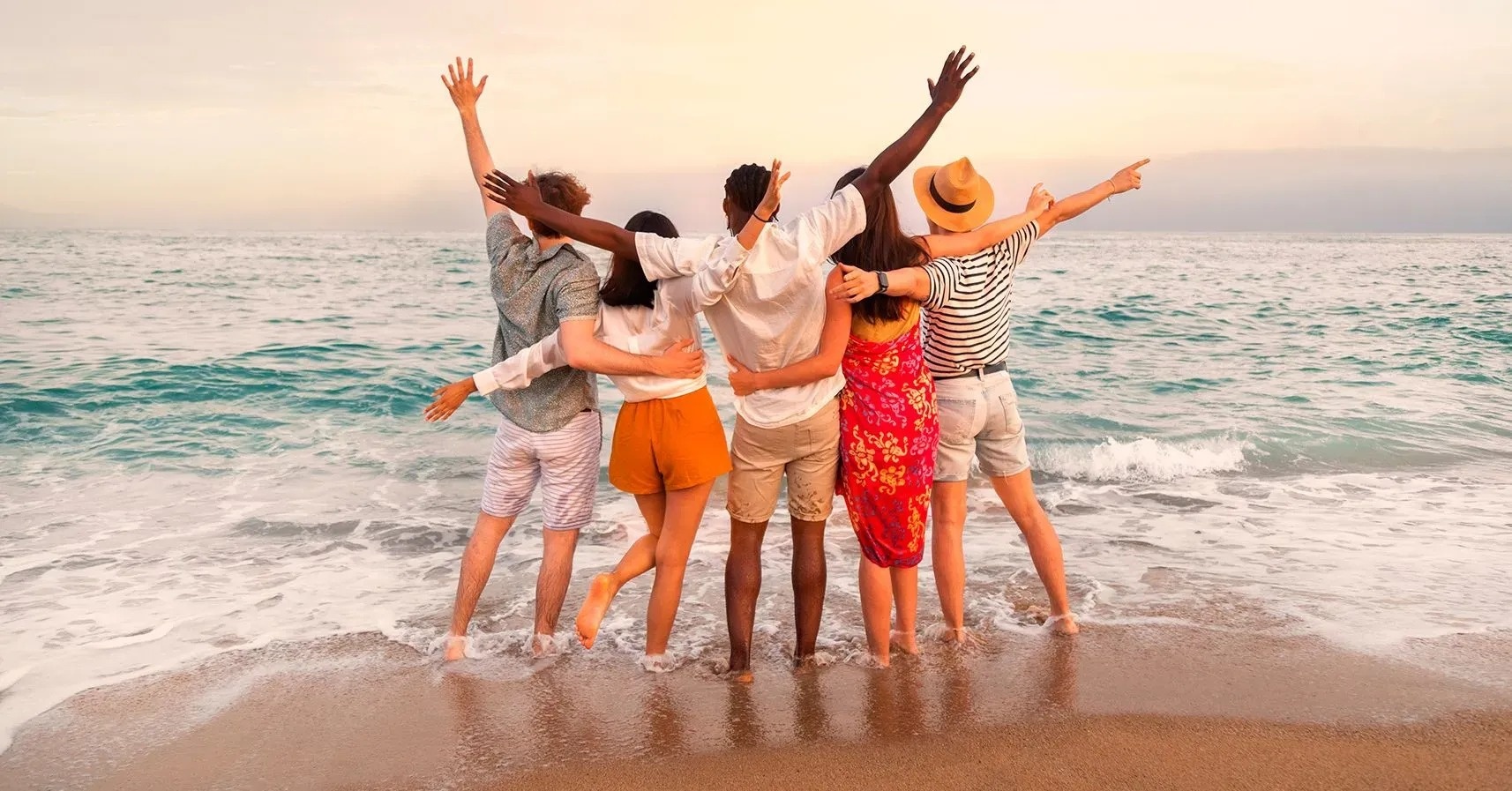 un grupo de personas de pie en la playa con los brazos en el aire
