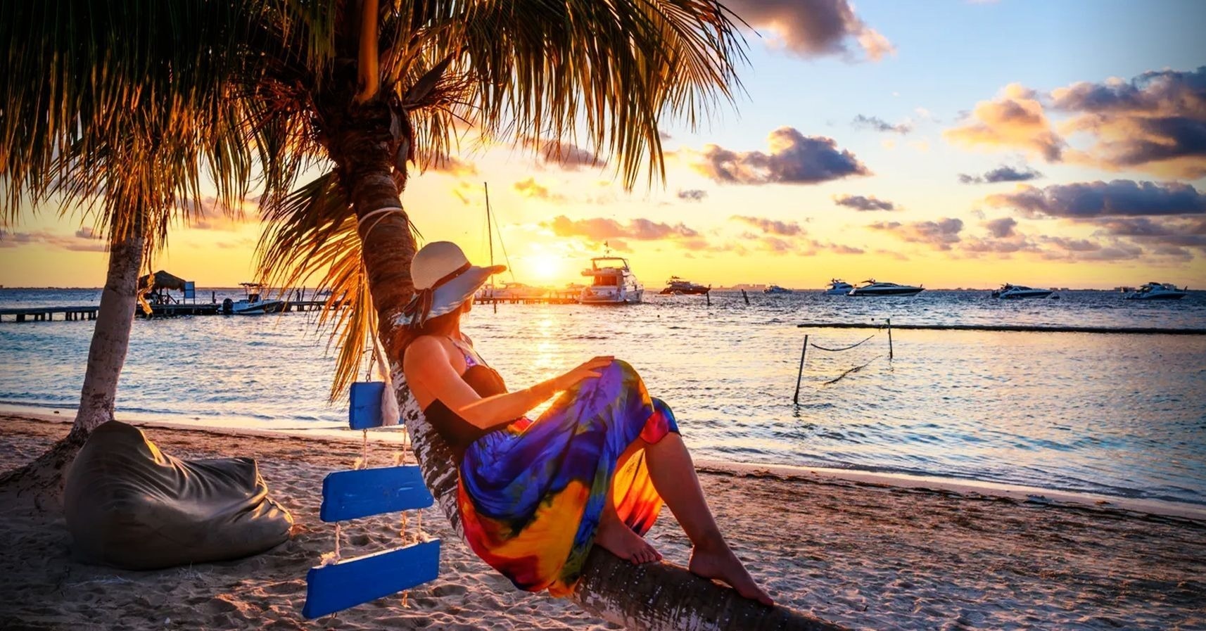una mujer se sienta en un columpio en la playa al atardecer