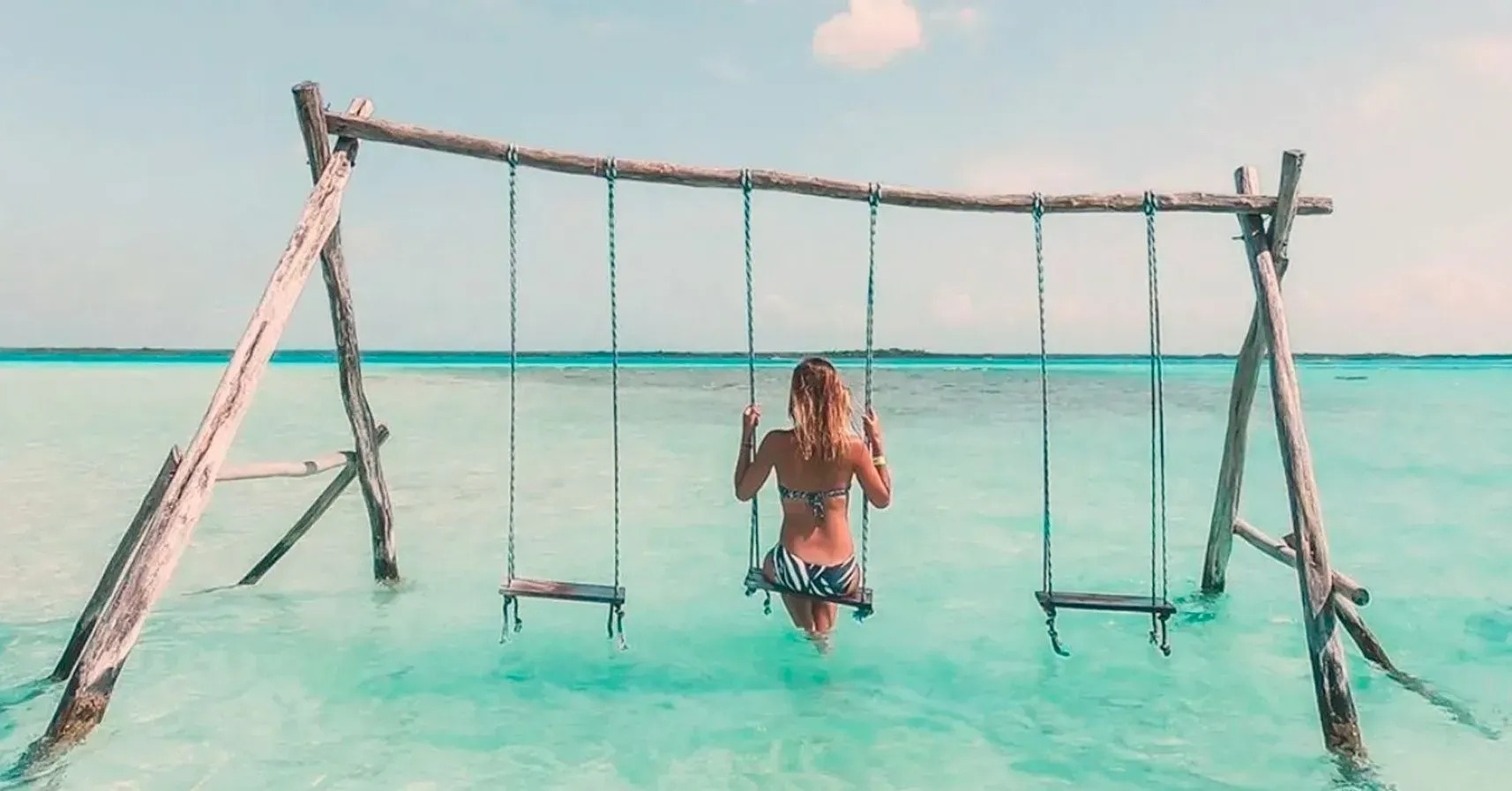 una mujer en bikini está sentada en un columpio en el océano