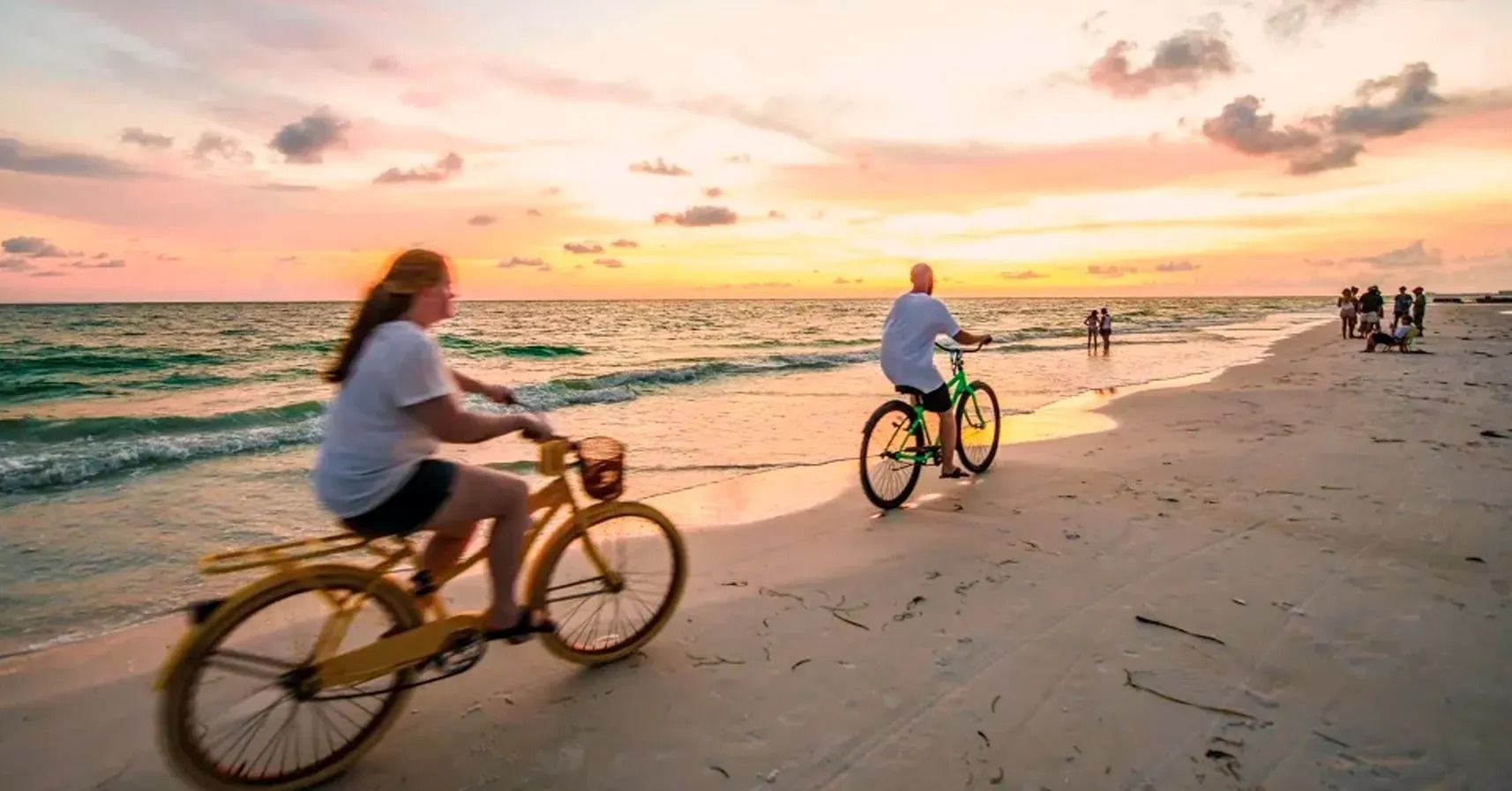 a man and a woman are riding bicycles on the beach at sunset