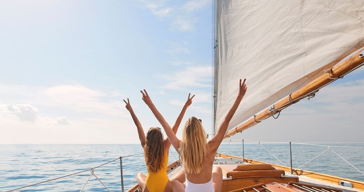 dos mujeres en trajes de baño amarillos y blancos están sentadas en un velero con los brazos en el aire