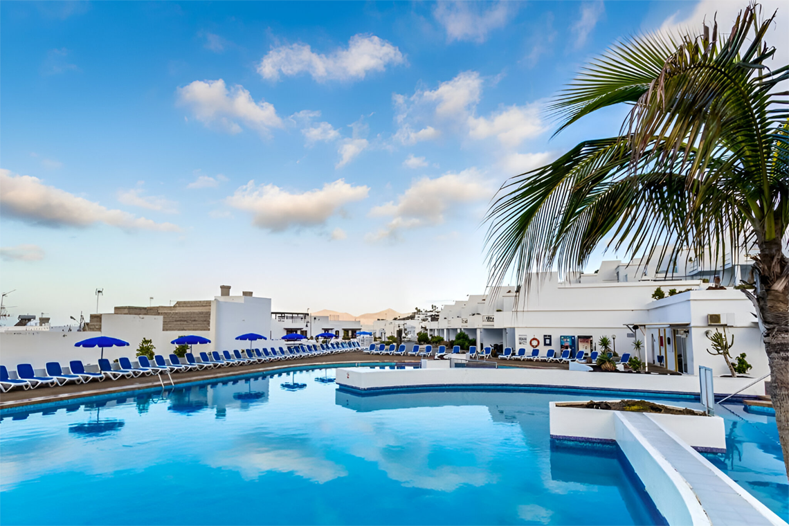 ein großer Swimmingpool mit blauen Sonnenschirmen und Palmen