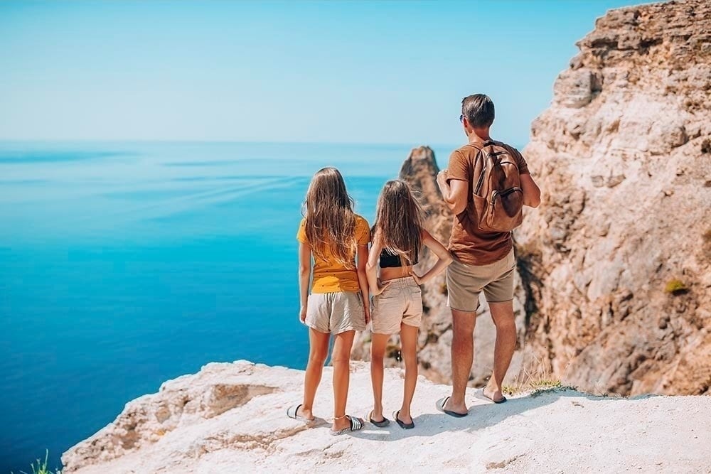 Vacaciones familiares: padre e hijas contemplando el océano desde la costa.