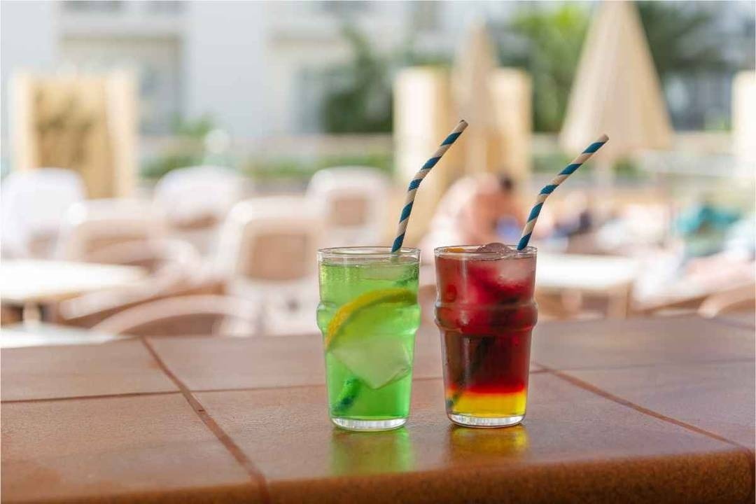 a glass of red liquid with a straw on the beach