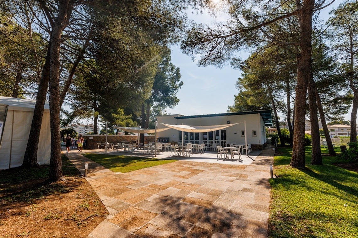 un patio con tavoli e sedie circondato da alberi e una tenda bianca