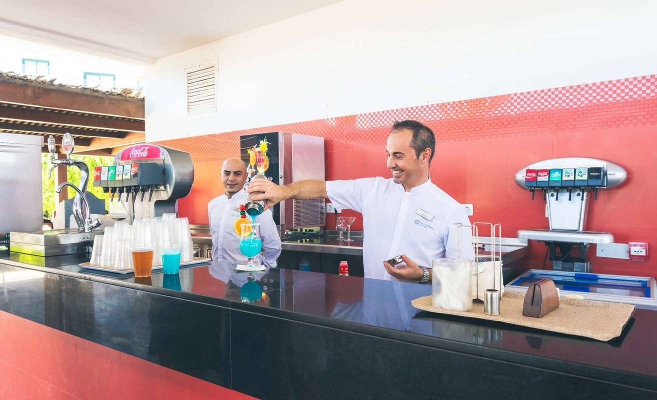 un barista versa una bevanda blu in un bicchiere accanto a un distributore di coca cola