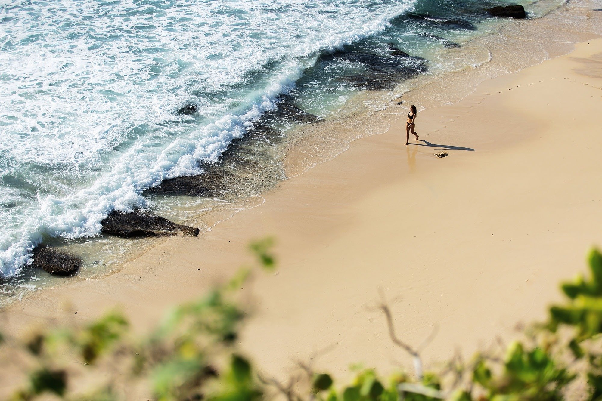 a woman in a bikini stands on a sandy beach near the ocean