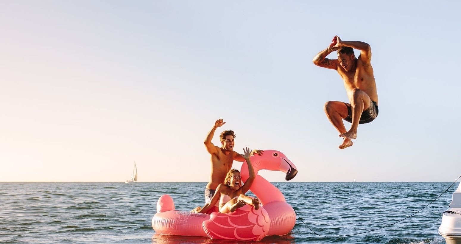 un hombre salta en el aire mientras está sentado en un flamingo inflable en el océano=s1900