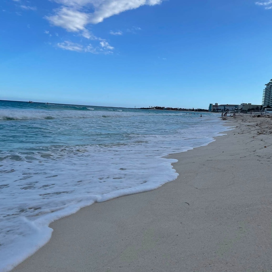 a beach with waves crashing on the sand and buildings in the background