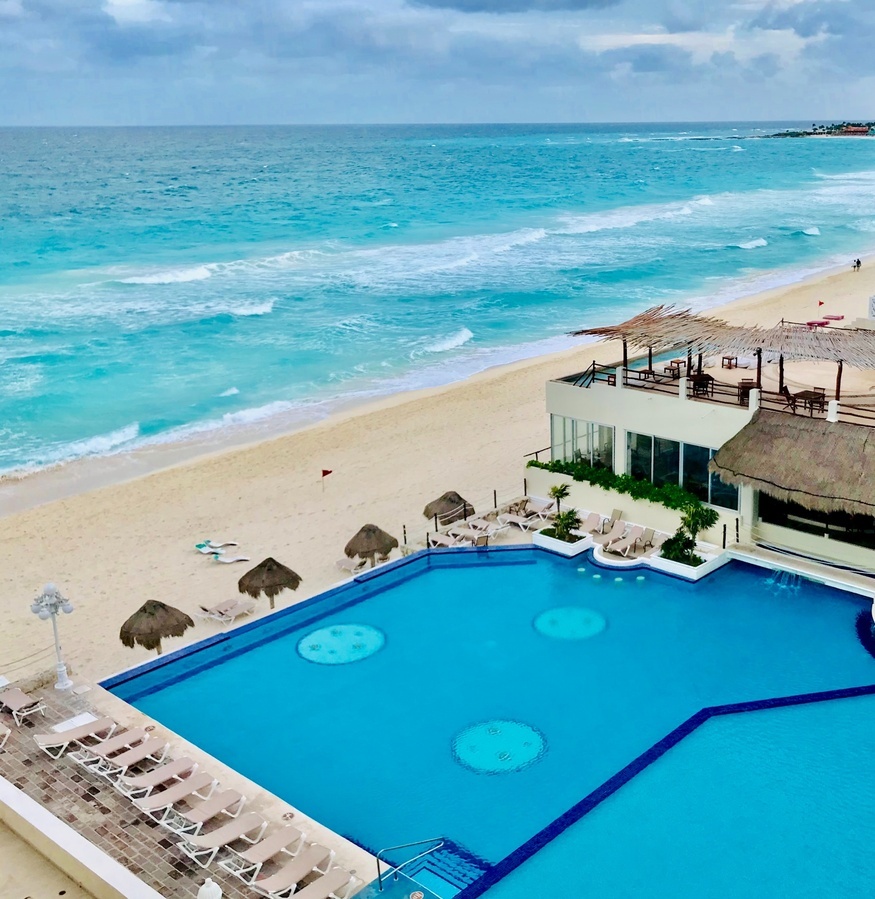 a large swimming pool surrounded by chairs and umbrellas on a beach