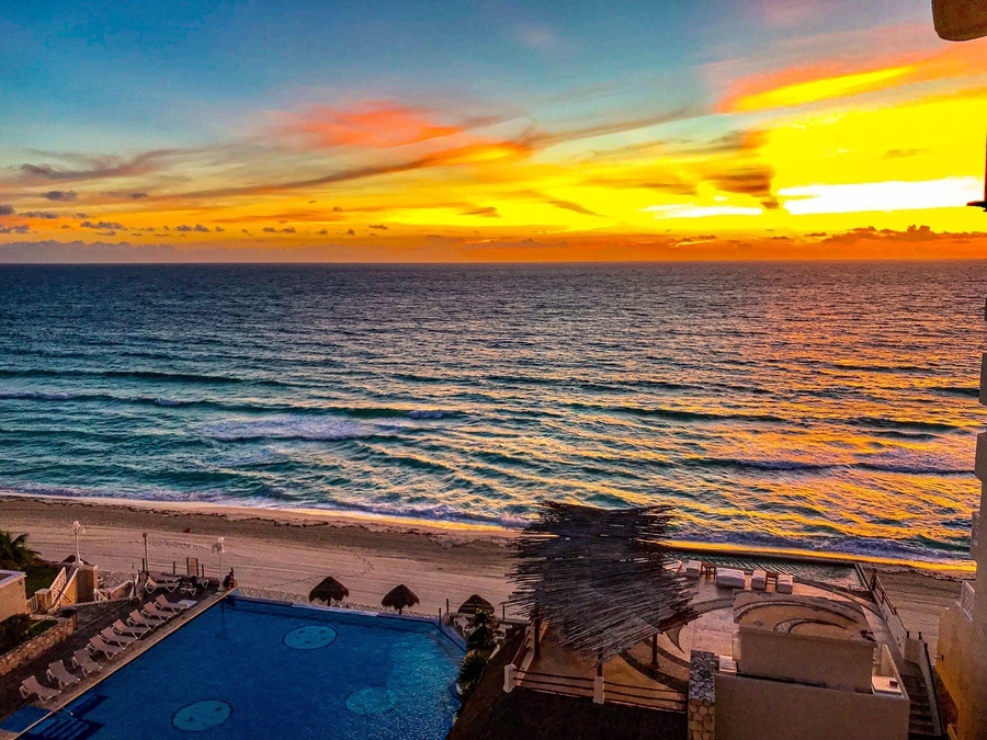 a sunset over the ocean with a swimming pool in the foreground
