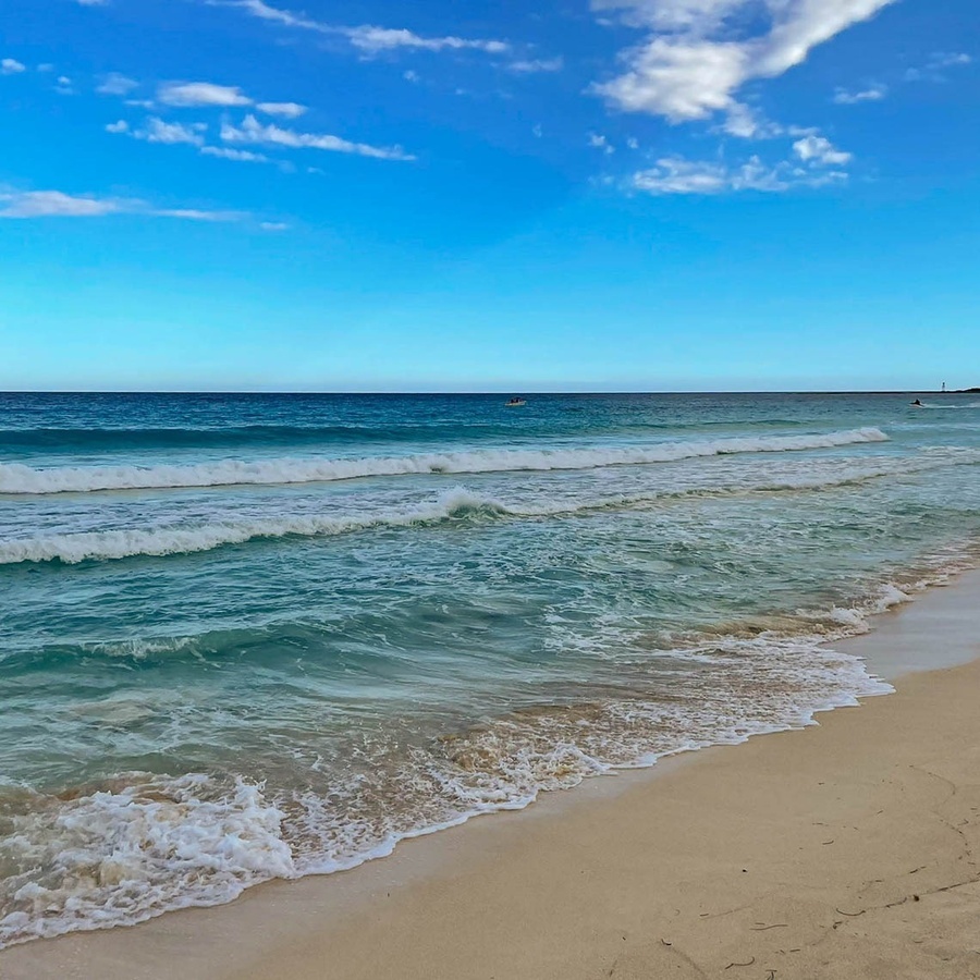 waves crashing on a sandy beach with a boat in the distance