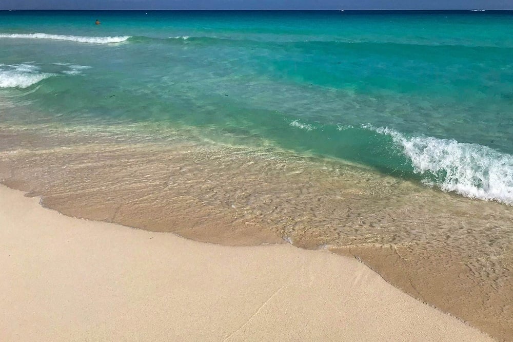 waves crashing on a sandy beach with a red buoy in the distance