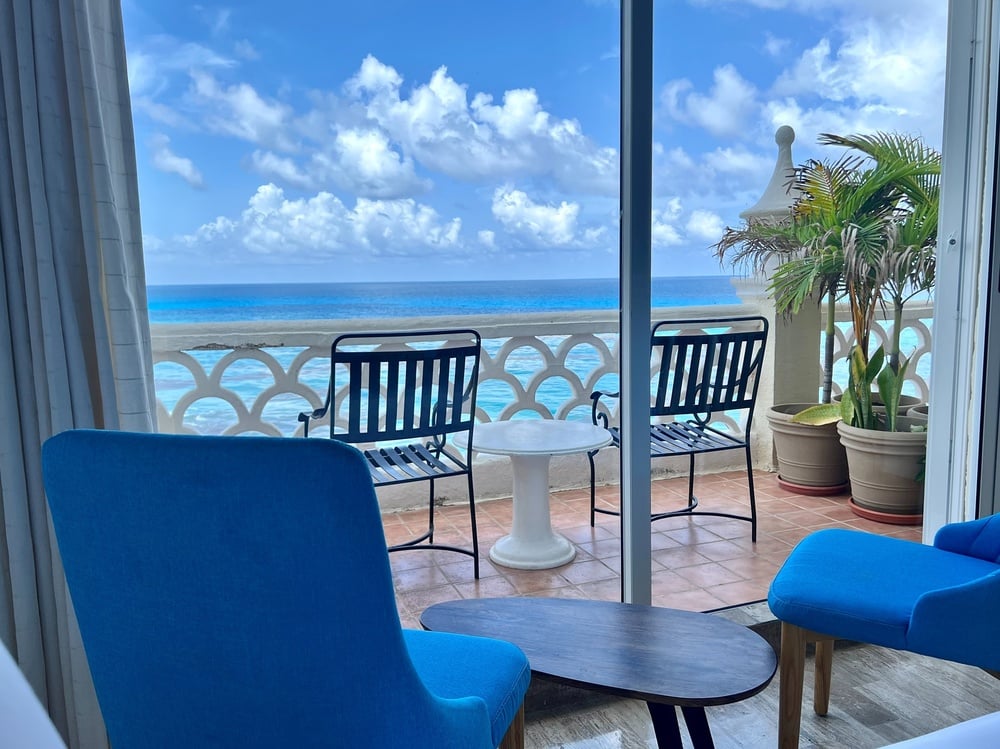 blue chairs and a table on a balcony overlooking the ocean