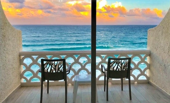 a balcony with two chairs and a table overlooking the ocean at sunset .
