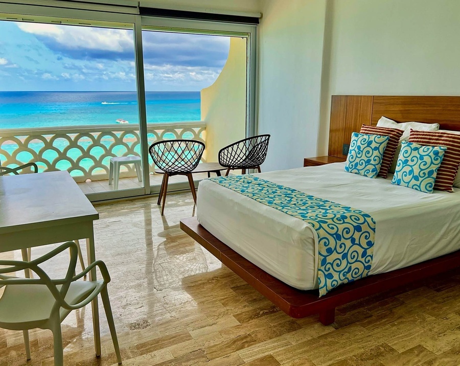 a hotel room with a bed and chairs with a view of the ocean