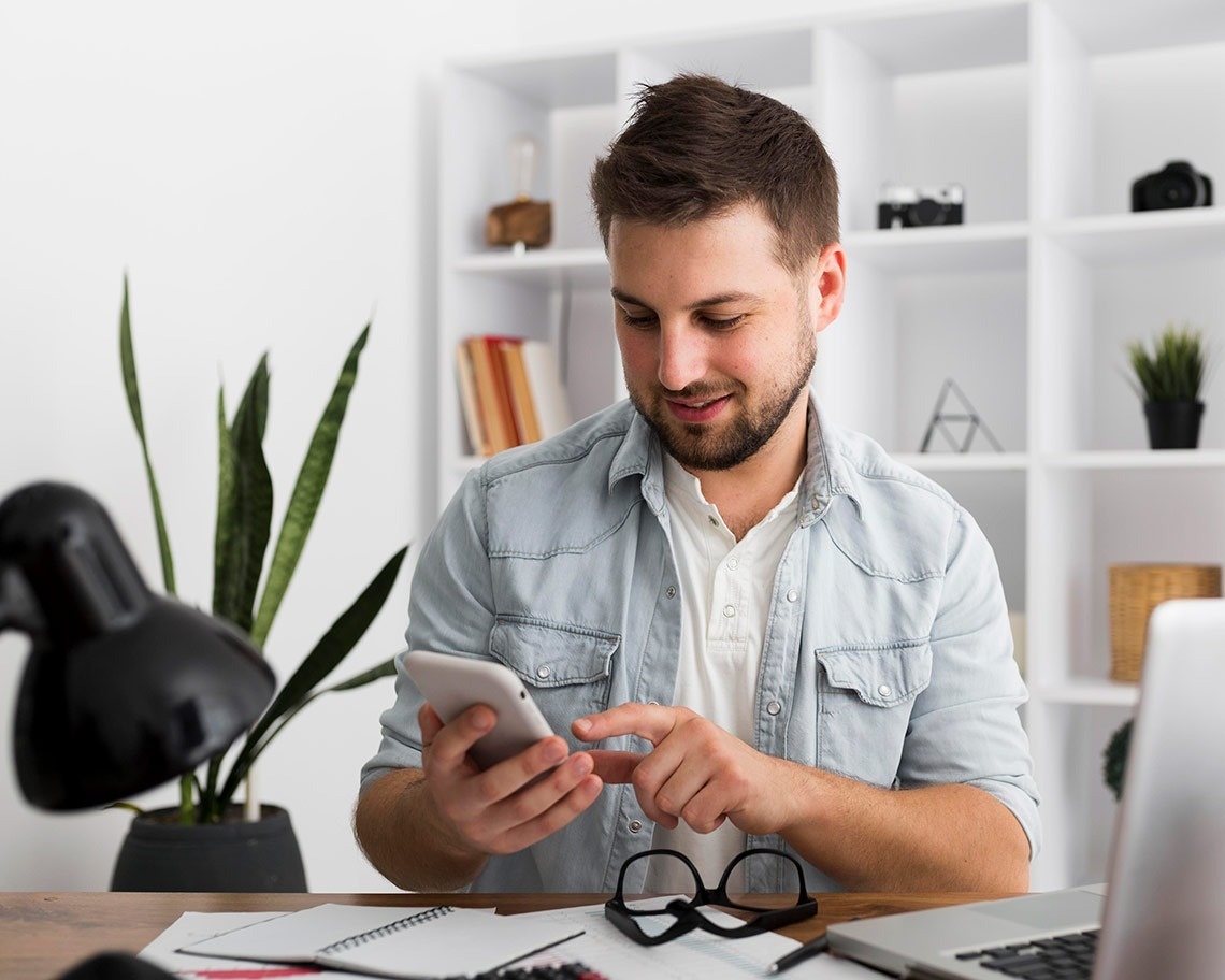 un hombre se sienta en una mesa mirando su teléfono celular