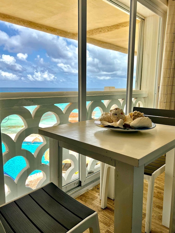 a teddy bear sits on a table in front of a window overlooking the ocean