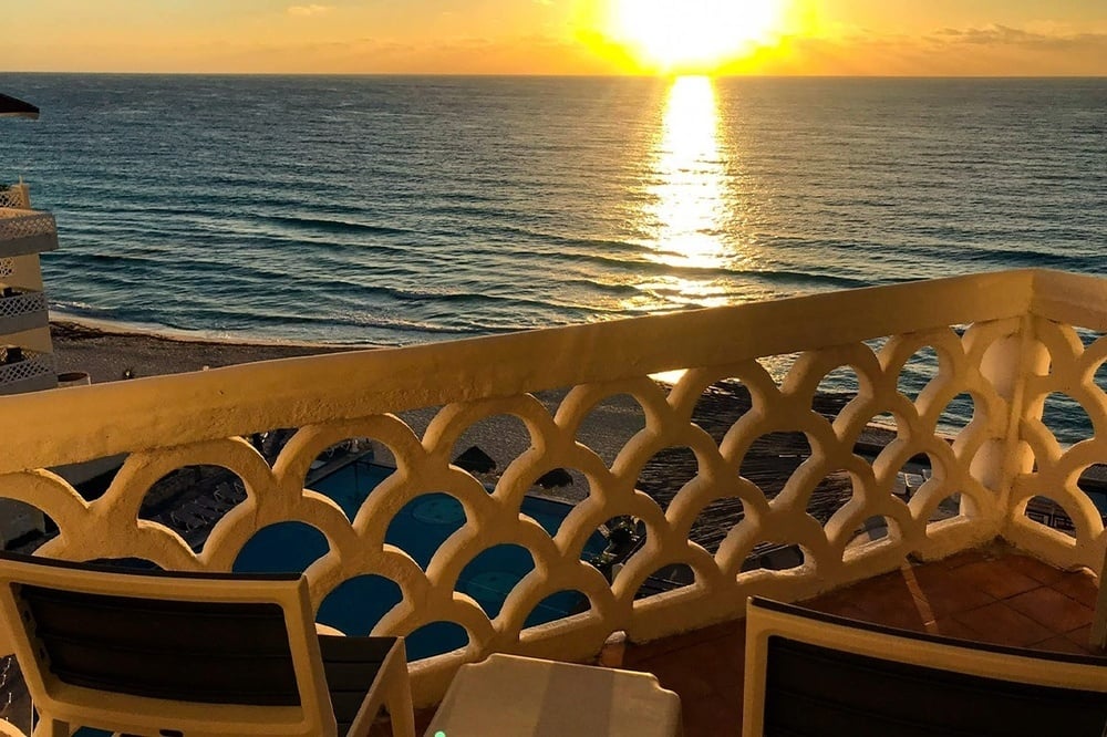 the sun is setting over the ocean from a balcony