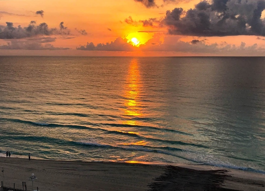 a sunset over the ocean with a beach in the foreground