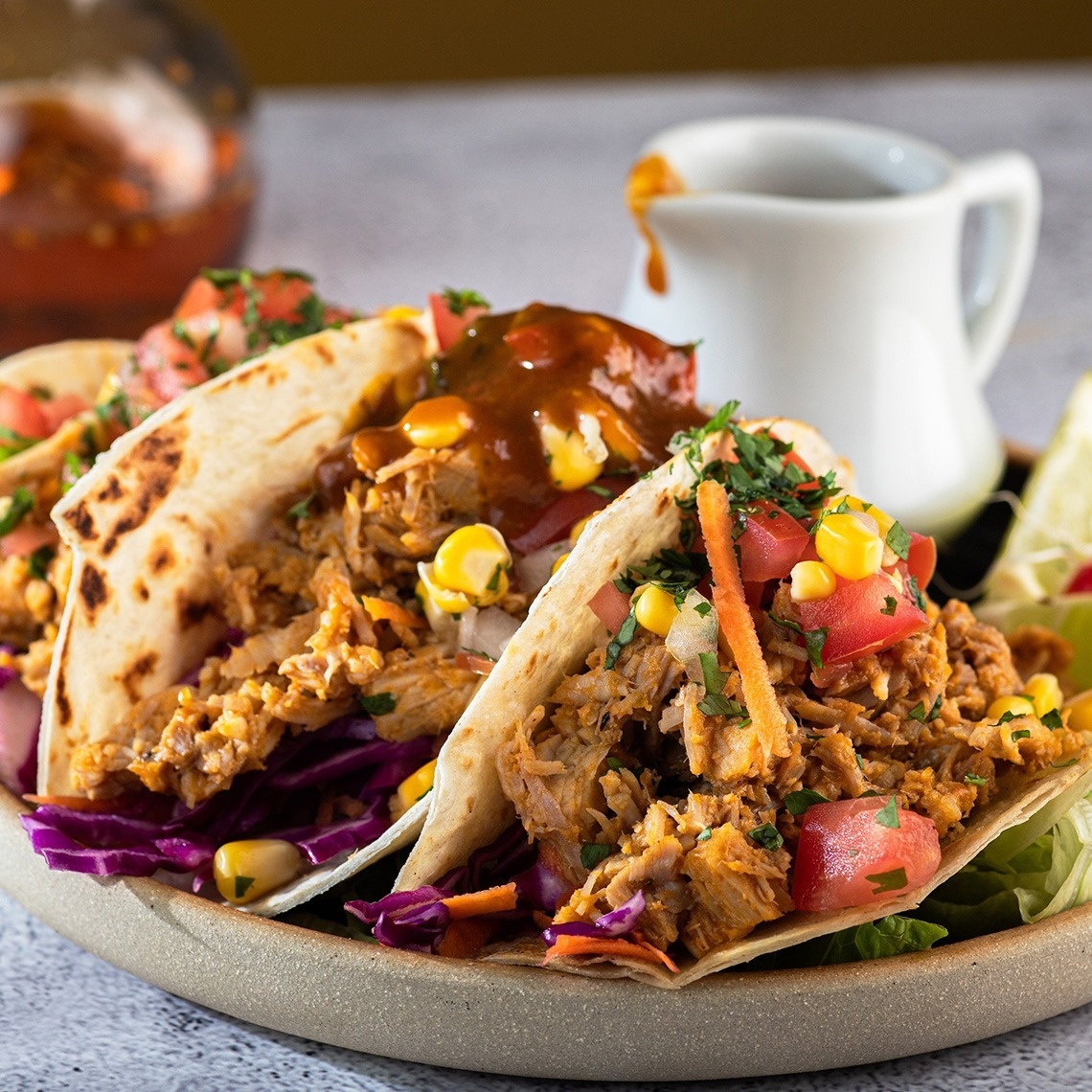 a plate of tacos with a pitcher of sauce in the background