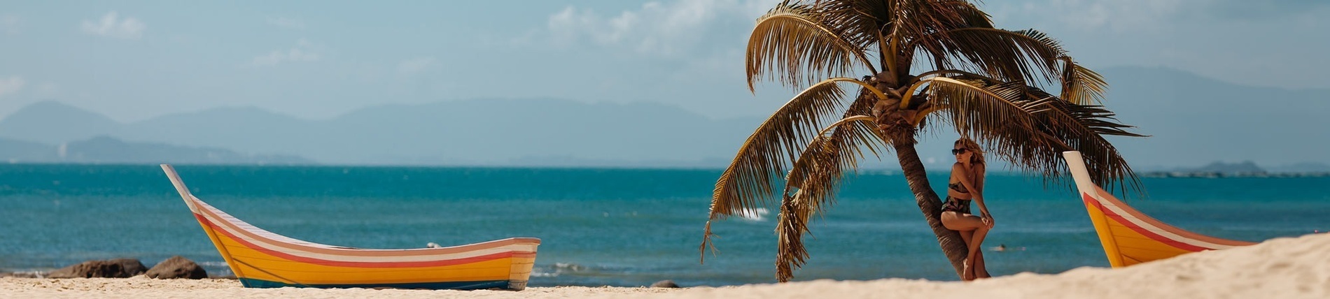 a woman leans against a palm tree on the beach